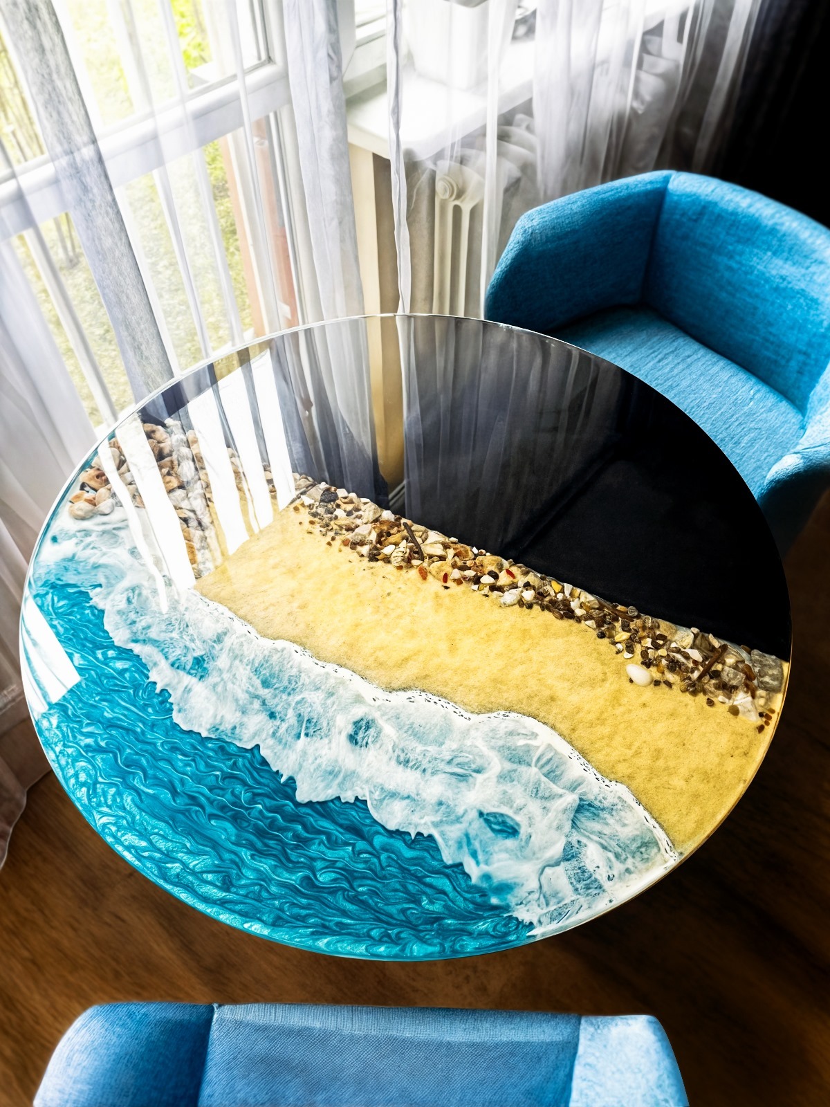 Okrągły blat stolika kawowego z żywicy epoksydowej, imitujący plażę i morze, z widocznymi kamieniami i falami. Wykonanie firmy z Żukowa.