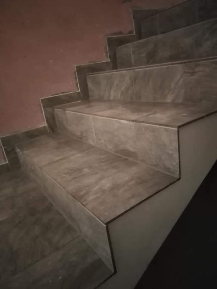 Schody wyłożone płytkami imitującymi marmur, z widocznymi fugami i fragmentem ściany w odcieniu różu.