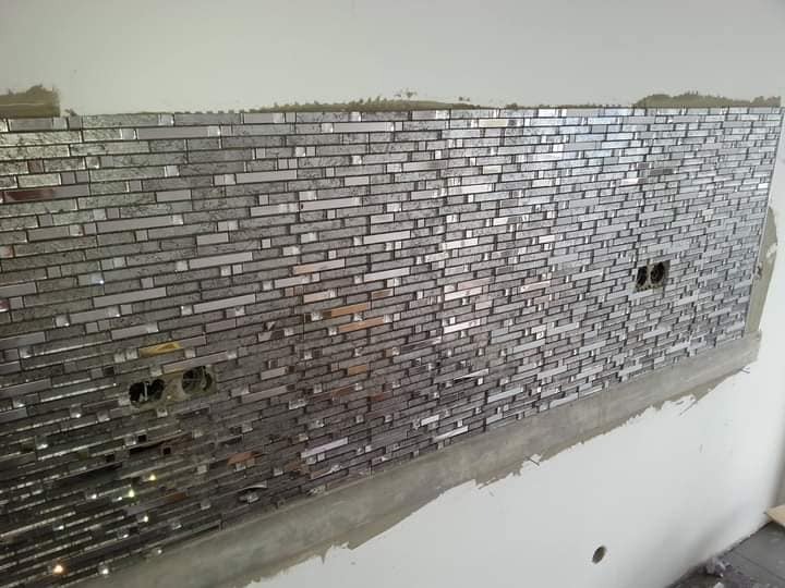 Ściana wyłożona mozaiką z lustrzanych płytek w trakcie montażu, widoczne puszki elektryczne i ślady zaprawy.