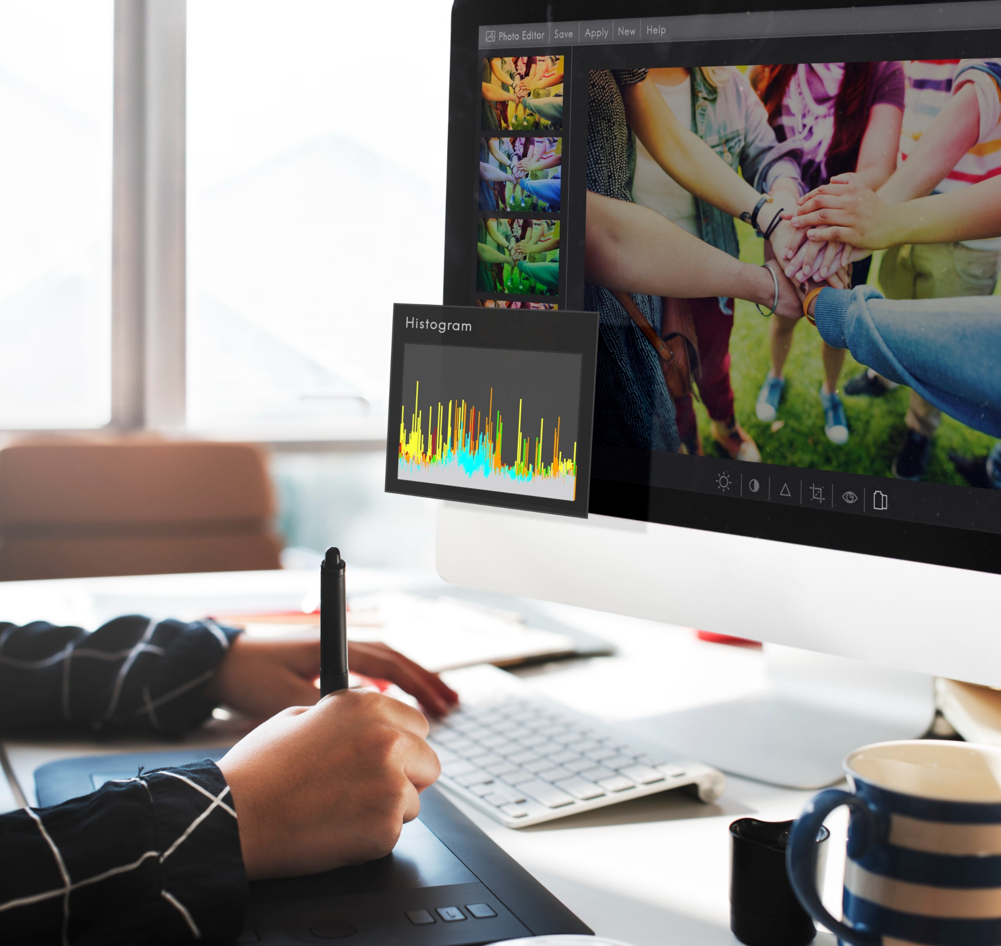Grafik pracuje na komputerze, używając tabletu graficznego i pióra, edytując zdjęcie z grupą osób trzymających się za ręce, widoczny histogram i paleta kolorów w programie graficznym.