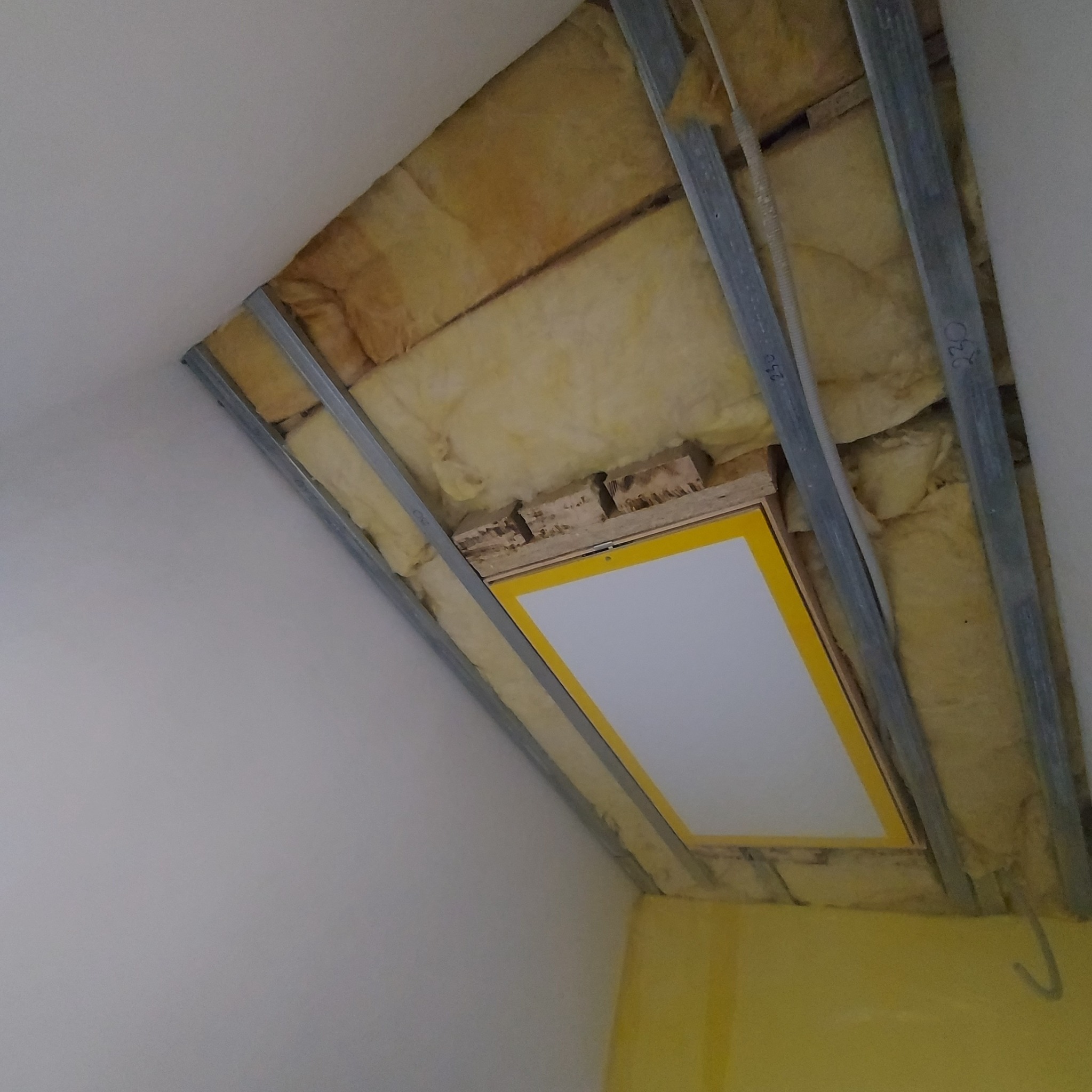 Sufit poddasza w trakcie izolacji: widoczne metalowe profile, wełna mineralna oraz klapa rewizyjna z żółtą ramką.