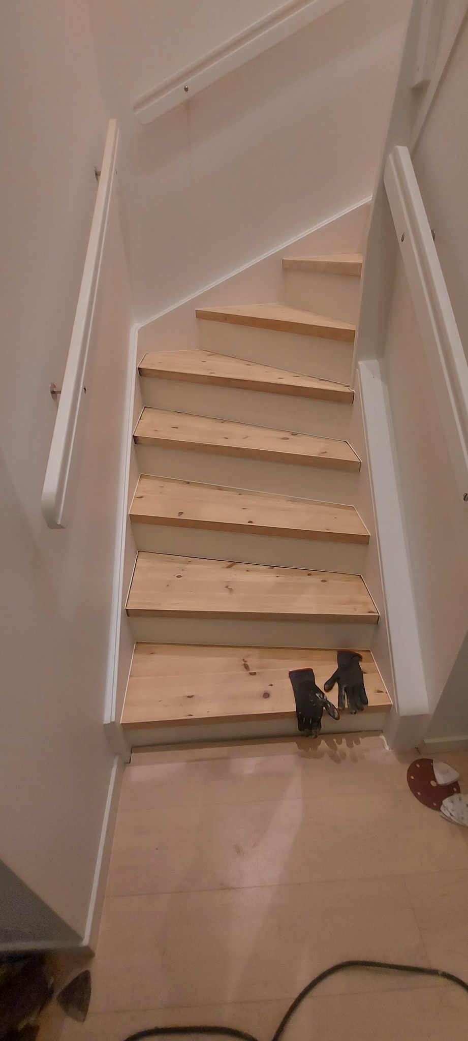 Jasne drewniane schody z białymi poręczami i czarnymi rękawicami roboczymi na dolnym stopniu, widok z góry.