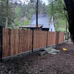 Vadym Boiko - Nowy, drewniany płot panelowy z czarnymi słupkami na tle leśnej działki w Warszawie. Widoczny fragment domu z szarym dachem. Świeżo wykonana instalacja.