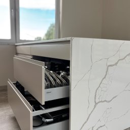 Meble KAVARI - Beżowa szafka kuchenna z blatem imitującym marmur, otwarte szuflady z systemem Blum, widoczne garnki i akcesoria kuchenne. Ujęcie z bliska, naturalne światło.