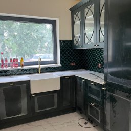 Alder Project - Nowoczesna kuchnia z ciemnozielonymi szafkami, białym blatem i zlewozmywakiem farmerskim. Uwagę przyciągają płytki w kształcie rybiej łuski i złota armatura.