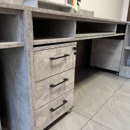 Alder Project - Szara, nowoczesna szafka biurowa z trzema szufladami na kółkach, z czarnymi uchwytami, widoczna pod kątem, na tle szarej podłogi. Klucz w zamku szuflady.