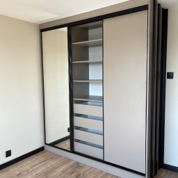 Alder Project - Beżowa szafa wnękowa z przesuwnymi drzwiami i lustrem, czarne akcenty, drewniana podłoga. Nowoczesny design, minimalistyczne wnętrze.