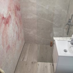 RENOVATION Piotr Kwiatkowski - Wykończona łazienka z drewnopodobnymi panelami podłogowymi, marmurowymi płytkami ściennymi i ścianą z efektem akwareli, widok z góry na umywalkę z szafką.