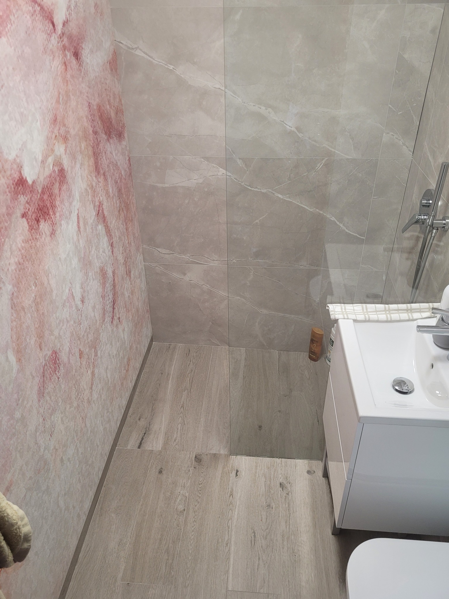 Wykończona łazienka z drewnopodobnymi panelami podłogowymi, marmurowymi płytkami ściennymi i ścianą z efektem akwareli, widok z góry na umywalkę z szafką.