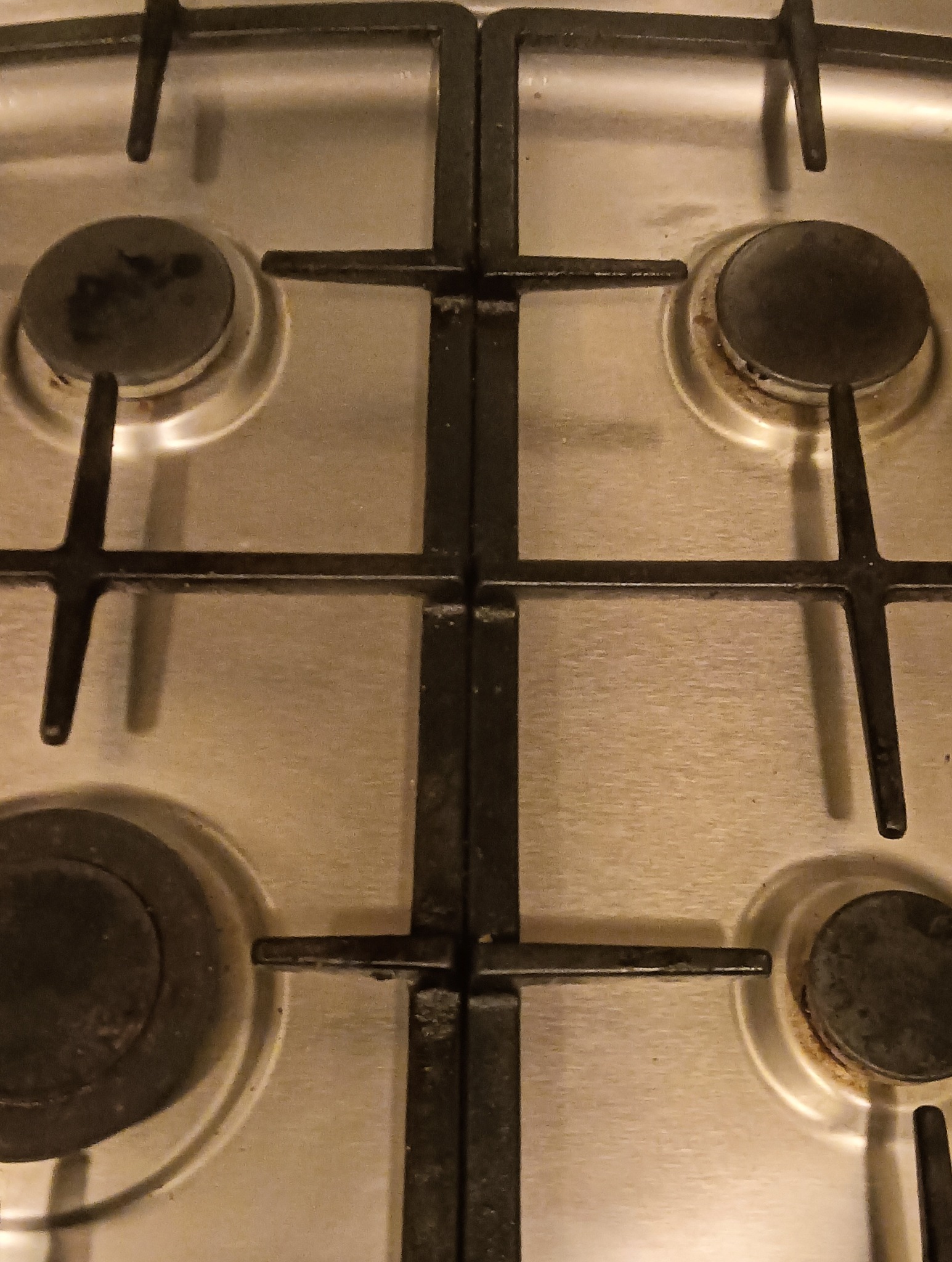 Brudna, metalowa płyta kuchenna z czterema palnikami, widoczny osad i zabrudzenia.