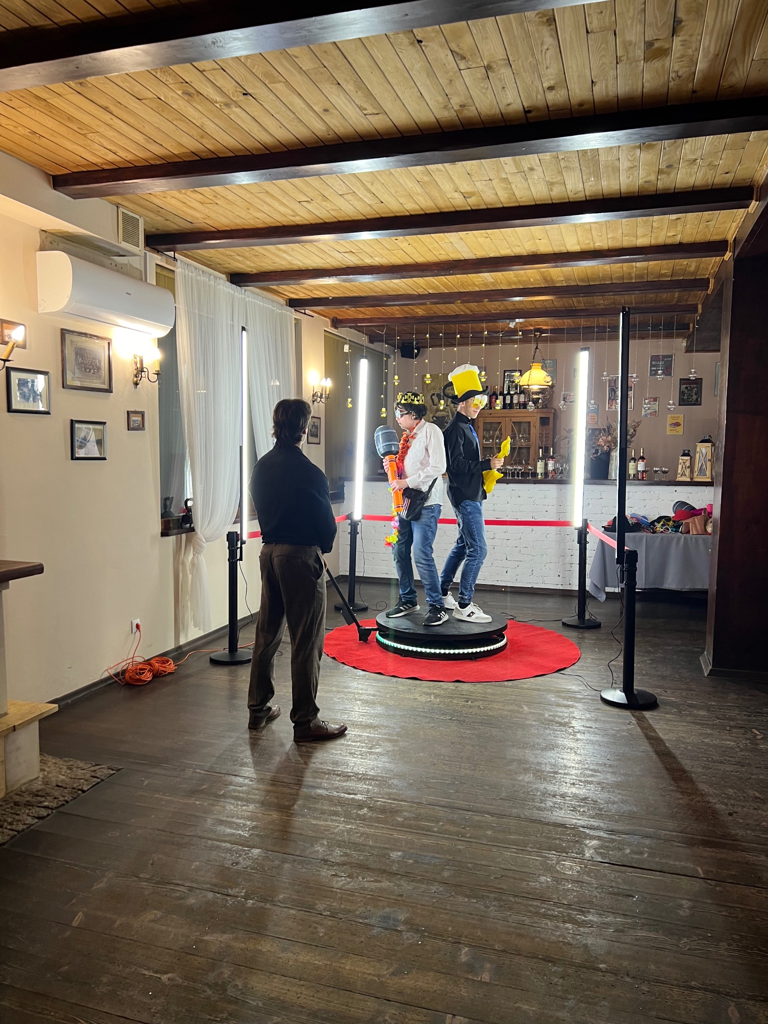 Dwóch mężczyzn w przebraniach pozuje na obrotowej platformie podczas imprezy z fotobudką w Tarnowskich Górach. Widoczny operator i dekoracje.