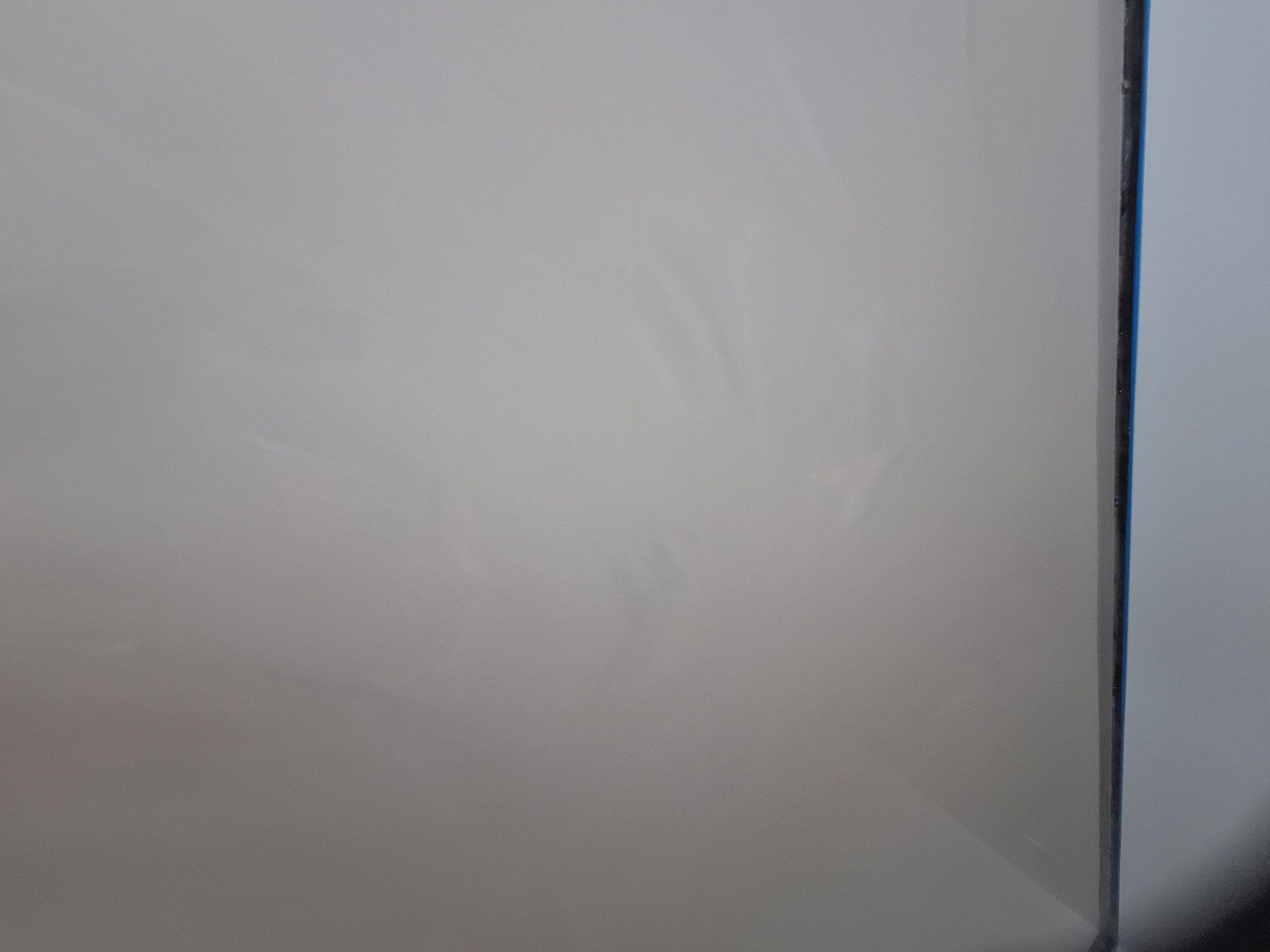 Jasnoszara, gładka powierzchnia ściany z delikatnymi smugami, widoczny fragment narożnika z niebieską taśmą ochronną.