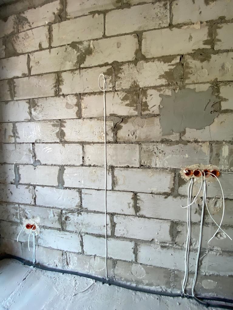 Niedokończona ściana z betonu komórkowego z trzema puszkami elektrycznymi i wystającymi przewodami, widoczna rura karbowana przy podłodze.