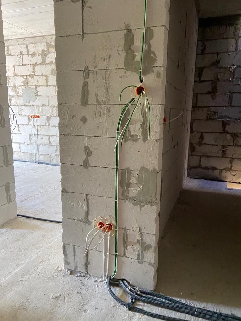 Wewnętrzne okablowanie elektryczne w surowym stanie, widoczne przewody w peszlach i puszkach instalacyjnych w ścianie z betonu komórkowego.