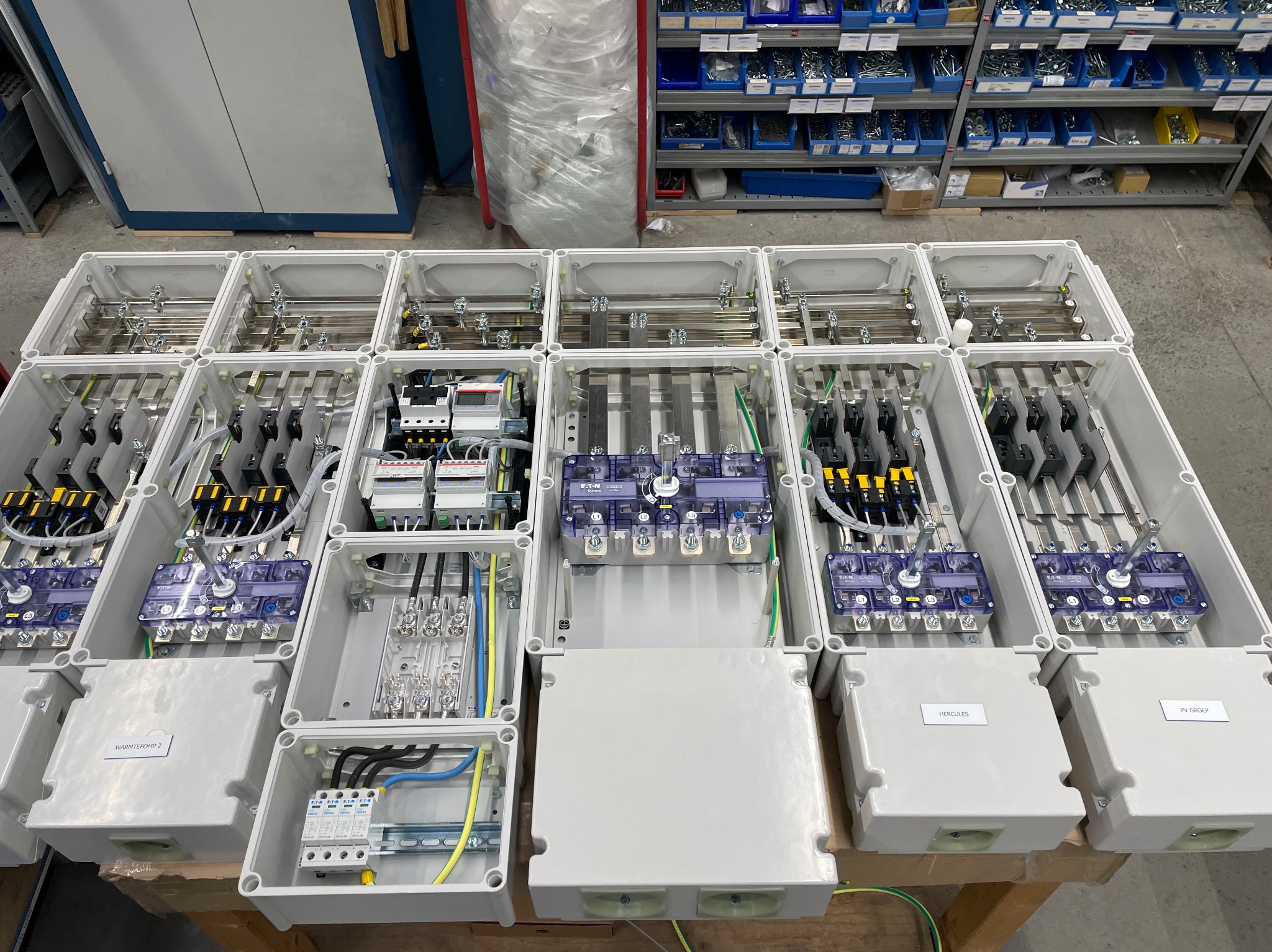 Rozdzielnice elektryczne w białych obudowach, widok z góry. Różne konfiguracje okablowania i zabezpieczeń. Część obudów zamknięta, część otwarta.