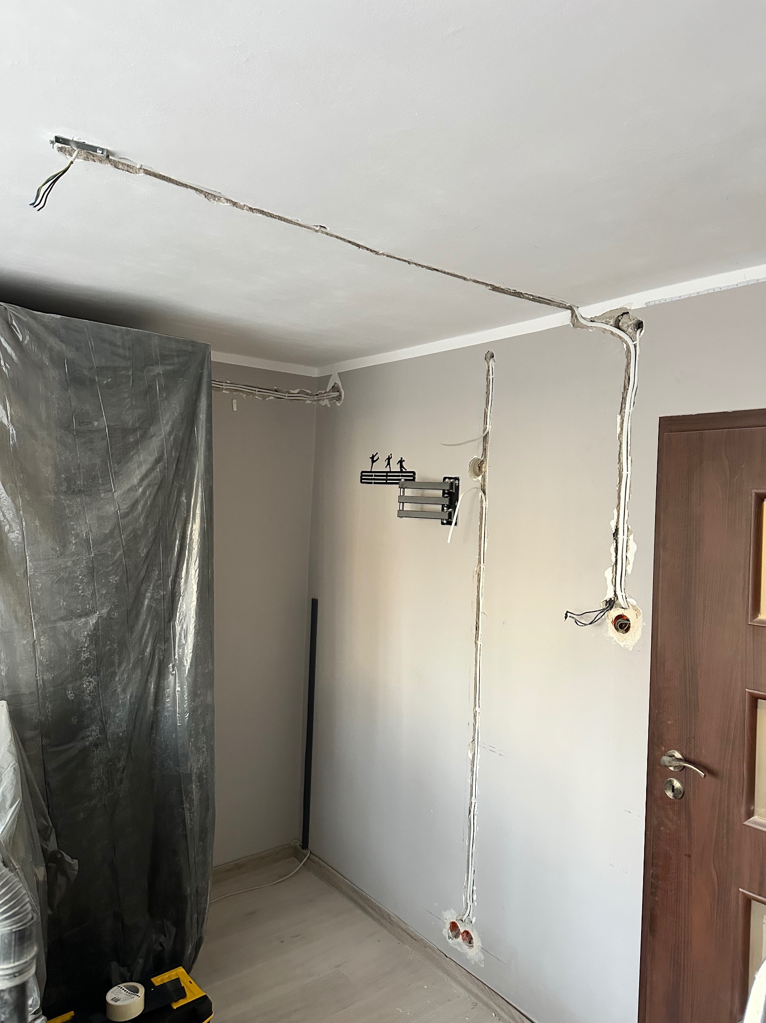 Wnętrze w trakcie prac elektrycznych: kable prowadzone w bruzdach ściennych i sufitowych, przygotowane gniazdka, folia ochronna na podłodze. Widoczne narzędzia.