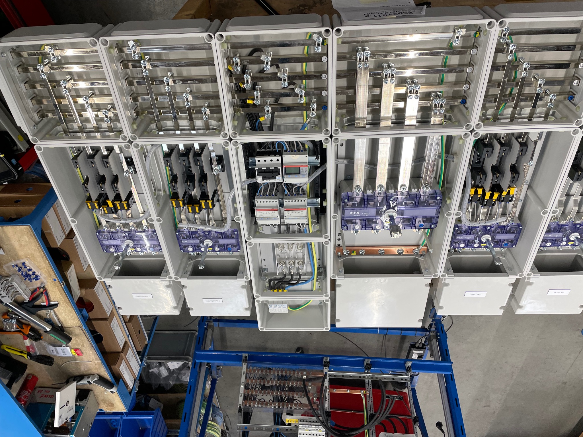 Rozdzielnice elektryczne w białych obudowach, widoczne kable, szyny i zabezpieczenia. Elementy instalacji elektrycznej w trakcie montażu.