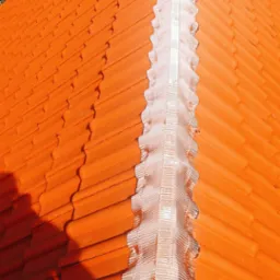 Pomarańczowy dach z dachówki ceramicznej z wykończeniem kalenicy w kolorze srebrnym, widziany z góry pod kątem, z fragmentem zieleni w tle.