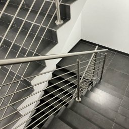 GLOBALSKILL SPÓŁKA Z OGRANICZONĄ ODPOWIEDZIALNOŚCIĄ - Nowoczesne schody z ciemnoszarą okładziną i balustradą ze stali nierdzewnej, widok z góry na fragment biegu schodowego.