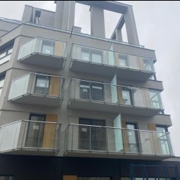 GLOBALSKILL SPÓŁKA Z OGRANICZONĄ ODPOWIEDZIALNOŚCIĄ - Nowoczesny budynek z balkonami z balustradami ze szkła i metalu. Ujęcie z dołu podkreśla architekturę budynku i minimalistyczny styl.