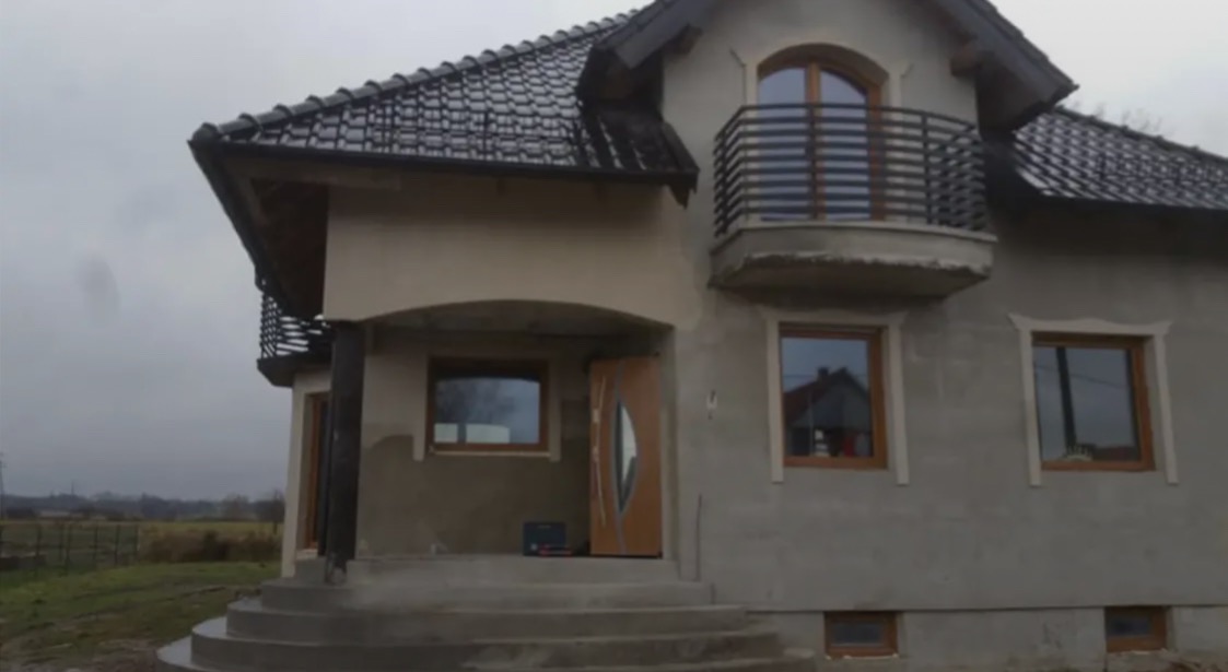 Dom w stanie surowym otwartym z metalową balustradą balkonową w Elblągu. Widoczne okna i drzwi z drewnianą stolarką. Elewacja w trakcie wykończenia.