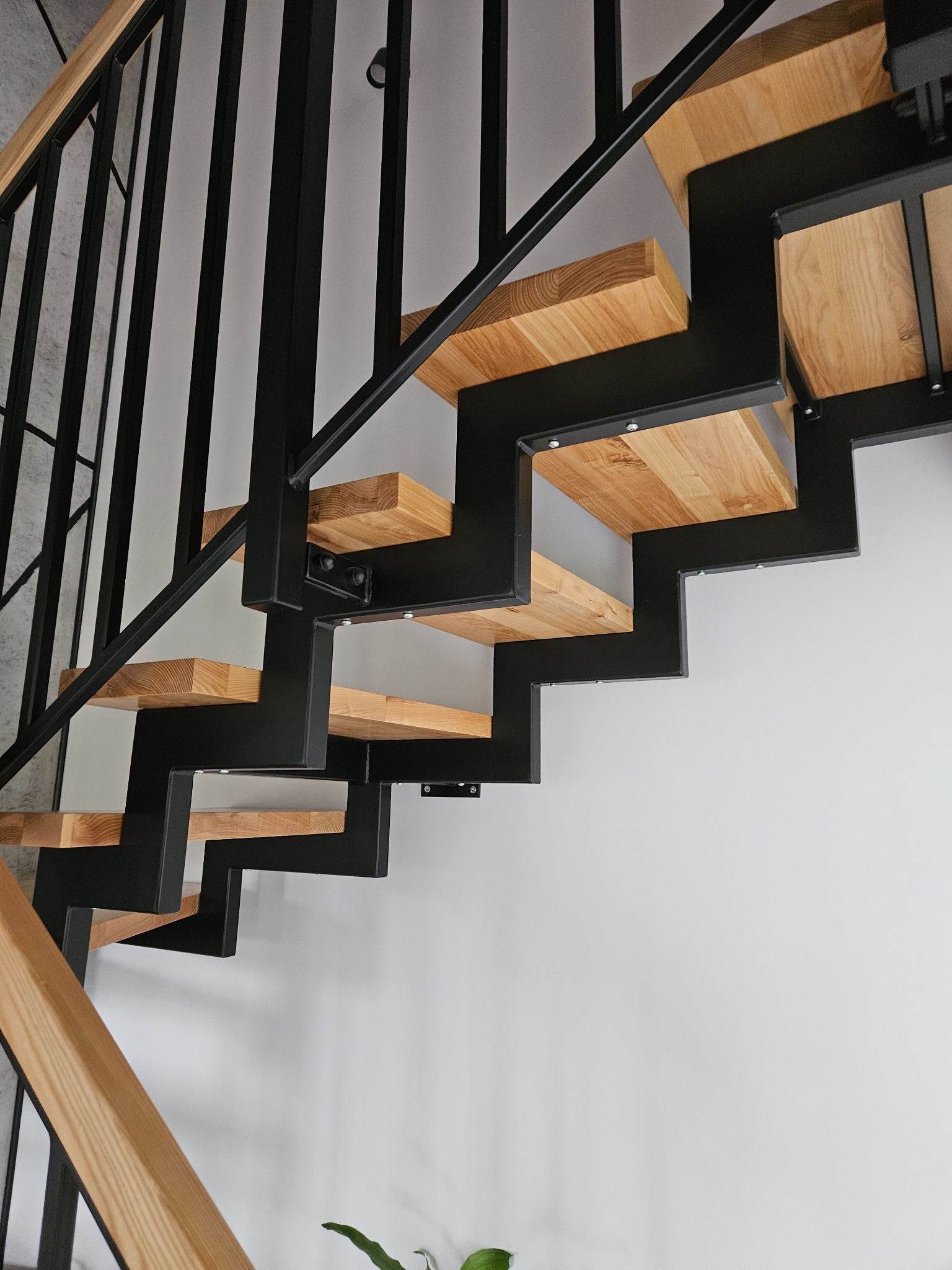 Nowoczesne schody metalowe z drewnianymi stopniami, czarna balustrada, minimalistyczny design, widok z dołu, jasne tło.