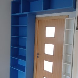 Michał Wojnar Jawor Meble - Niebieska zabudowa regałowa nad drzwiami, z półkami po bokach, na tle parkietu. Widoczna drewniana ościeżnica i fragment białego regału po prawej.