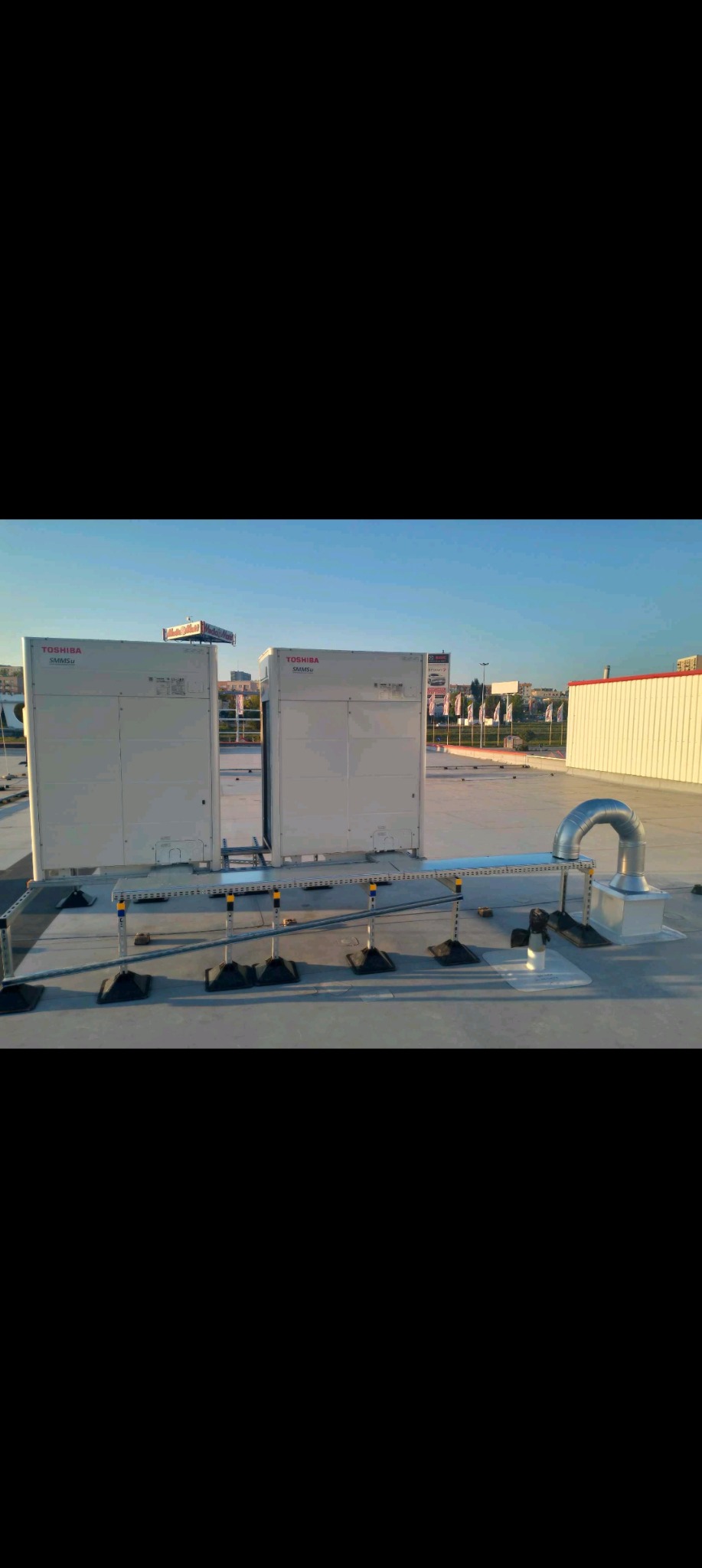 Dwa agregaty klimatyzacyjne Toshiba SMMSu zainstalowane na dachu budynku, połączone rurociągiem wentylacyjnym z wykorzystaniem konstrukcji wsporczej z żółtymi elementami stabilizującymi.