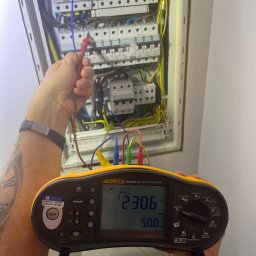 Automatyka Energetyka Zabezpieczenia - Elektryk mierzy napięcie w rozdzielnicy za pomocą miernika Fluke 1664 FC. Widoczne przewody, bezpieczniki i wynik pomiaru na wyświetlaczu.