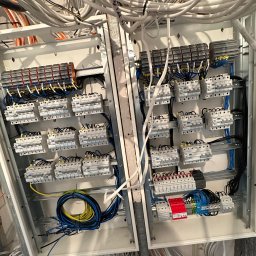 Automatyka Energetyka Zabezpieczenia - Rozdzielnia elektryczna w trakcie montażu: widoczne zabezpieczenia, przewody i listwy zaciskowe. Surowy stan, kable u góry.