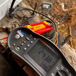 Automatyka Energetyka Zabezpieczenia - Miernik Fluke 1664 FC pokazuje wynik pomiaru instalacji elektrycznej, wskazując napięcie 243.8V i częstotliwość 50.0Hz. Widoczne kable i narzędzia.