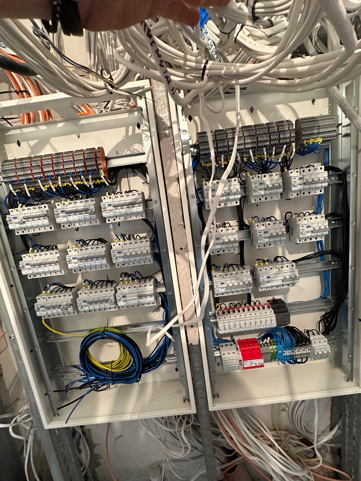 Rozdzielnia elektryczna w trakcie montażu: widoczne zabezpieczenia, przewody i listwy zaciskowe. Surowy stan, kable u góry.