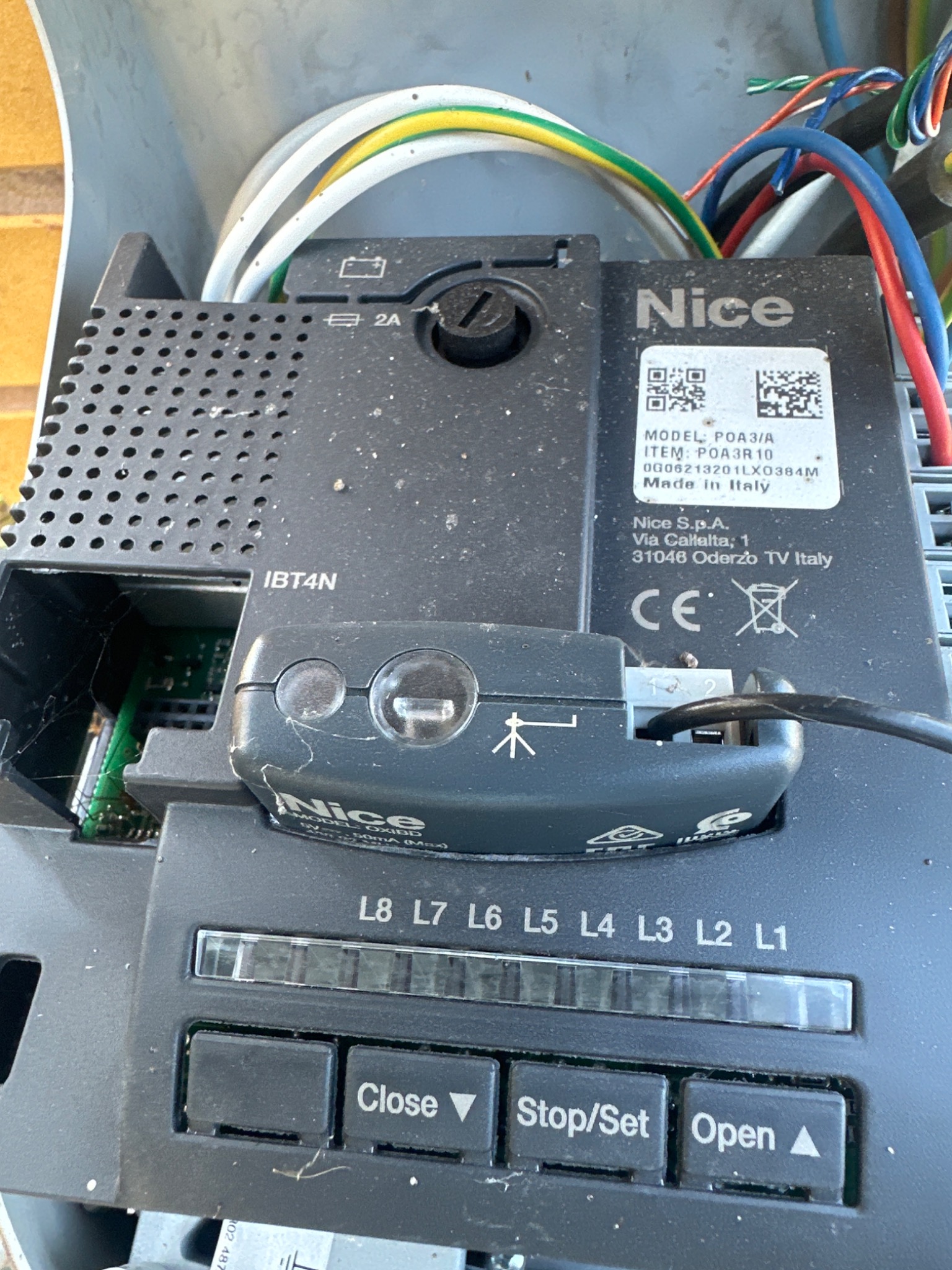 Sterownik bramy Nice POA3/A z widocznymi przyciskami Close, Stop/Set i Open oraz diodami L1-L8. Widoczne przewody i elementy elektroniki.