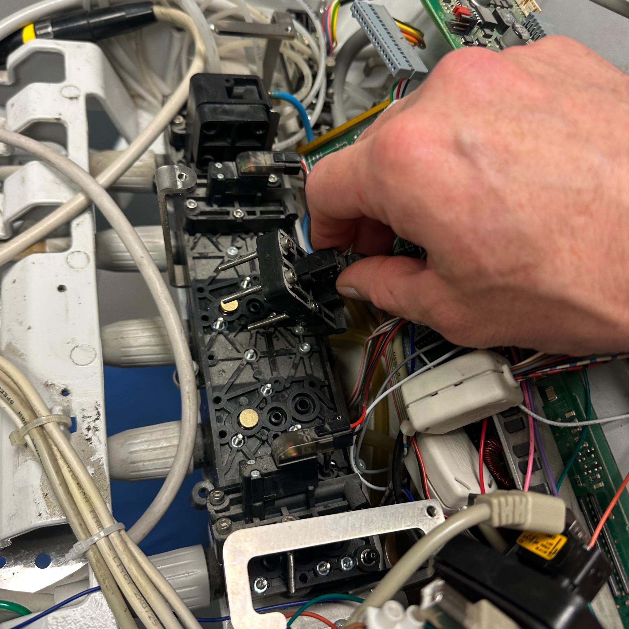 Czarna skrzynka elektryczna z przewodami i ręką podczas montażu elementu, widok z góry, ostre światło. Detal z instalacji elektrycznej, etap prac.