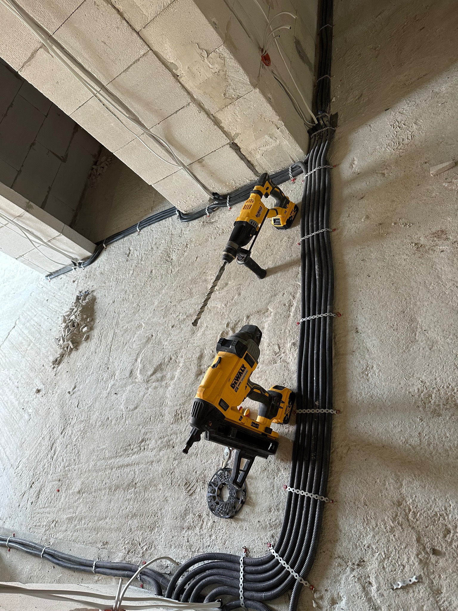 Kable w peszlach mocowane do surowej ściany z użyciem narzędzi DeWalt. Widoczne wiercenia i otwory. Etap prac instalacyjnych w nowym budynku.