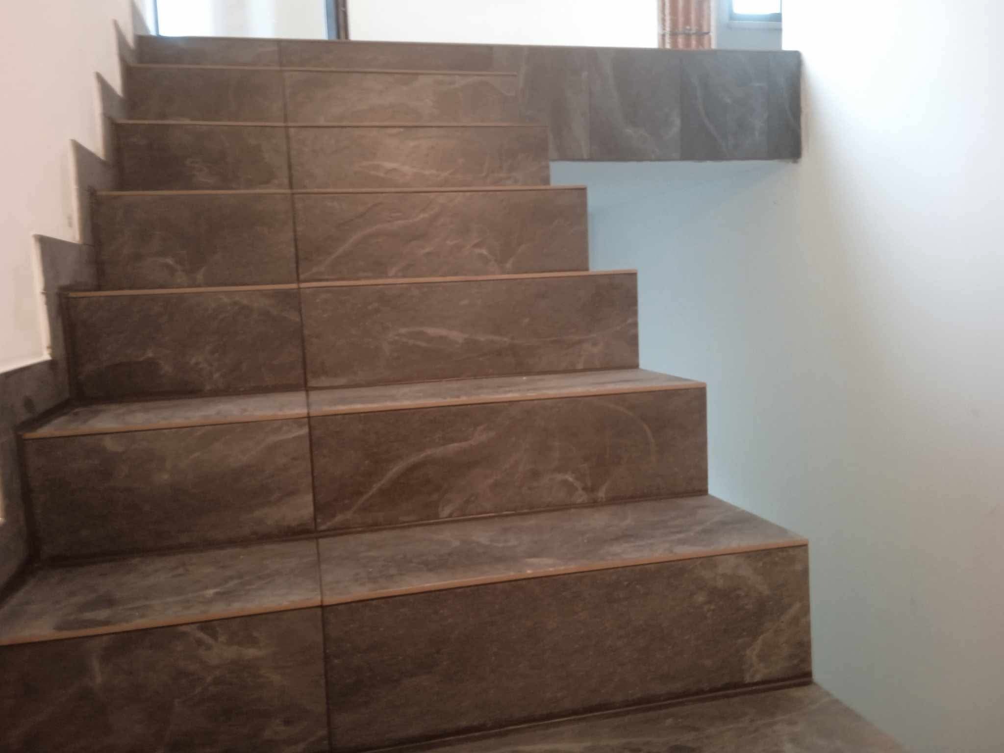 Schody wyłożone brązowymi płytkami imitującymi marmur, z widocznymi fugami i krawędziami schodów, na tle białej ściany.