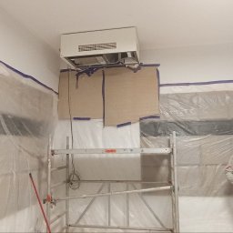 Dmytro kokoshko - Przygotowania do remontu: zabezpieczone folią okna, rusztowanie, klimatyzator pod sufitem, mężczyzna w tle. Etap prac przed malowaniem ścian.