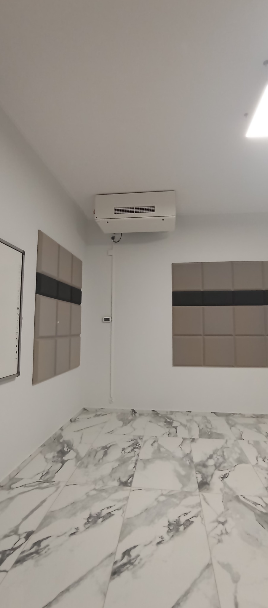 Nowoczesne wnętrze z marmurową podłogą, panelami ściennymi w odcieniach beżu i szarości oraz klimatyzatorem. Minimalistyczny design, jasne ściany.