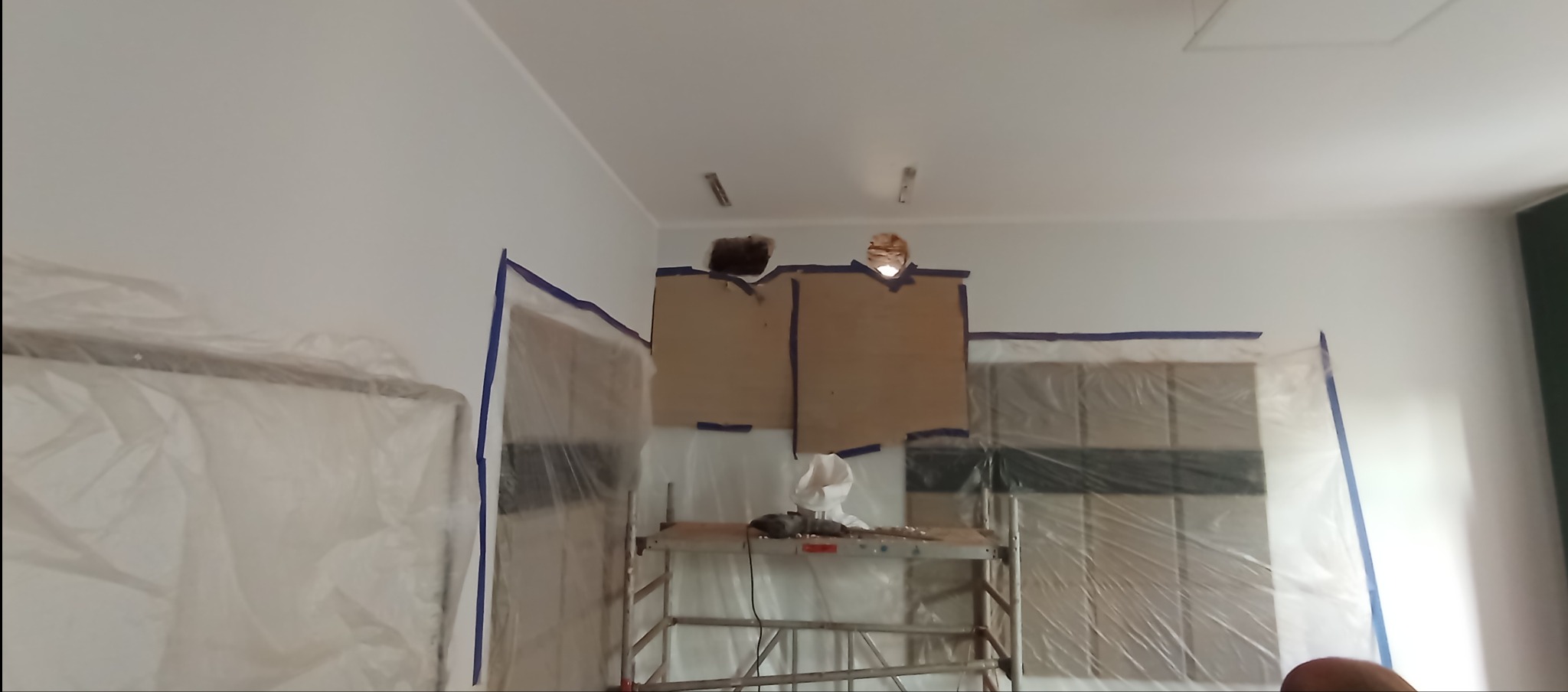 Przygotowania do remontu: zabezpieczone folią drzwi, kartonowe osłony na ścianie, rusztowanie. Widoczne ślady po instalacji elektrycznej.