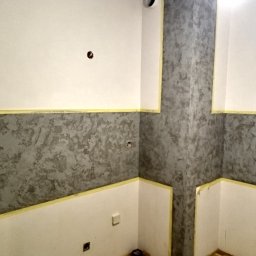 PROF-REMONT-EXPRES BOHDAN KOMARYNSKYI - Wnętrze w trakcie malowania dekoracyjnego z użyciem taśmy malarskiej, widoczne puste otwory na gniazdka elektryczne i rury.