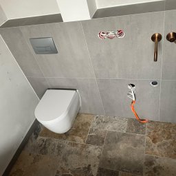 PROF-REMONT-EXPRES BOHDAN KOMARYNSKYI - Wisząca toaleta z szarą płytką ścienną, miedziana armatura, instalacja elektryczna wystająca ze ściany i brązowa płytka podłogowa.