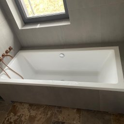 PROF-REMONT-EXPRES BOHDAN KOMARYNSKYI - Nowoczesna, prostokątna wanna w obudowie z szarych płytek, z miedzianą armaturą i oknem dachowym.