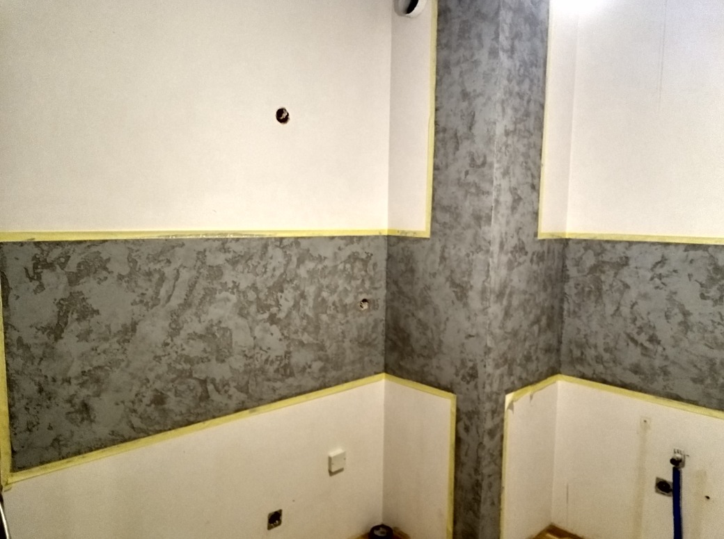 Wnętrze w trakcie malowania dekoracyjnego z użyciem taśmy malarskiej, widoczne puste otwory na gniazdka elektryczne i rury.