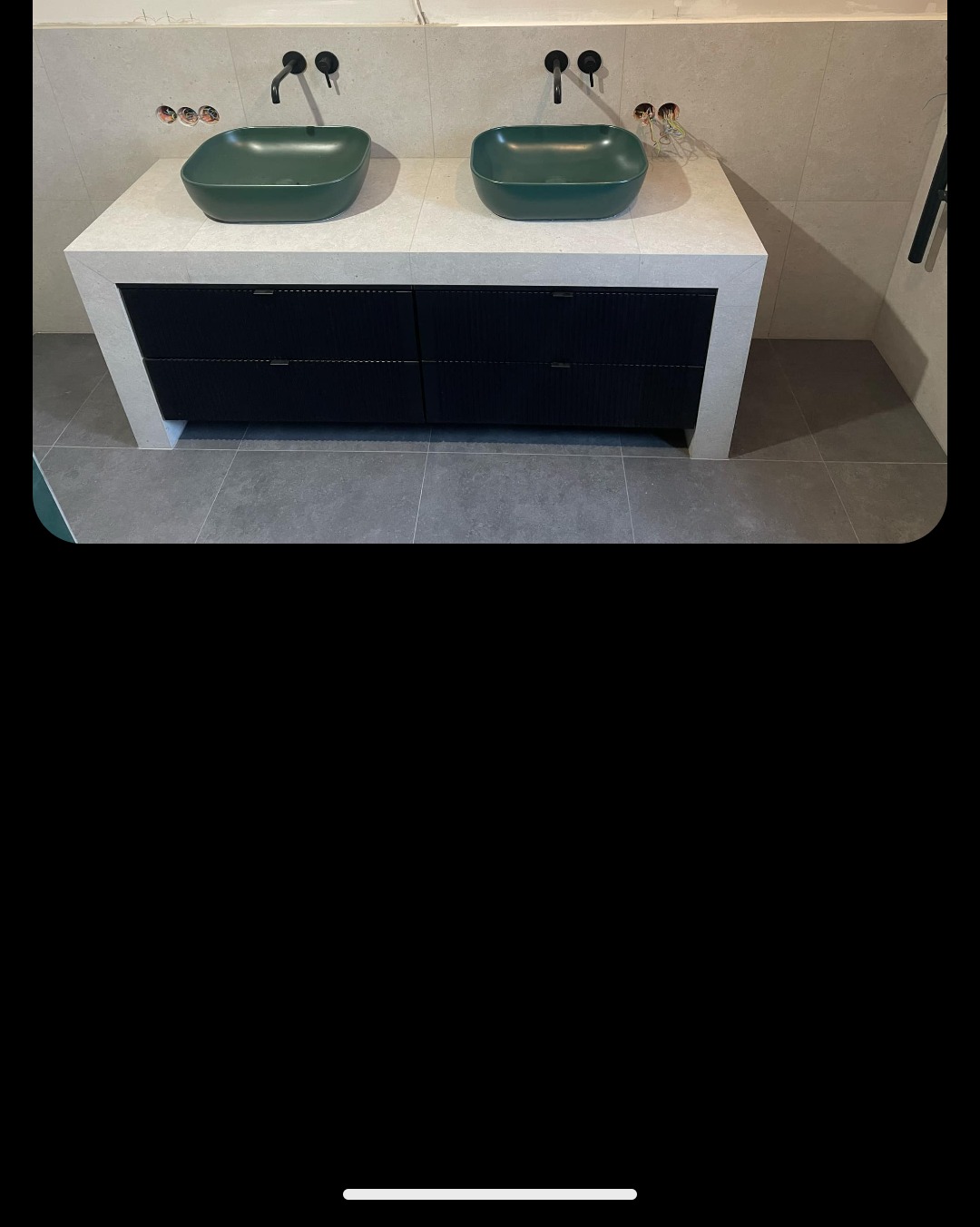 Nowoczesna łazienka z dwoma zielonymi umywalkami nablatowymi o kwadratowym kształcie, zamontowanymi na białym blacie z czarnymi szufladami o fakturze drewna, czarne baterie umywalkowe, szare płytki...