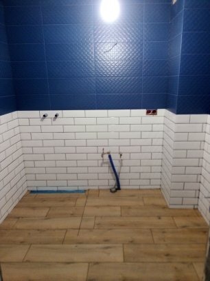 Łazienka w trakcie remontu: położone panele podłogowe imitujące drewno, białe kafelki typu metro na ścianach do połowy wysokości, górna część ścian wyłożona ciemnoniebieskimi płytkami z delikatnym...