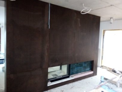 Montaż ściany z płyty karton gips z wnęką na kominek z wykończeniem z płytek ceramicznych, widoczne kable pod sufitem i surowe wykończenie pomieszczenia.