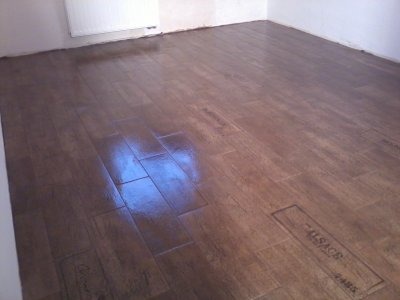 Ułożona podłoga z brązowych paneli imitujących drewno, widoczne odbicie światła i logo 'ALSACE PARQUET' na jednym z paneli.