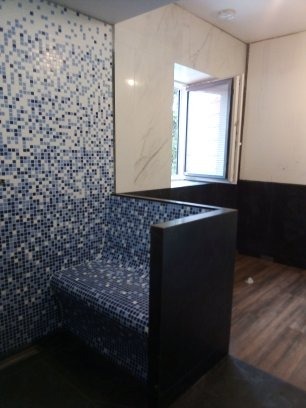 Mozaika w odcieniach bieli i błękitu zdobi ścianę i siedzisko w nowoczesnej łazience z oknem. Ciemne panele na dole ściany i drewnopodobna podłoga.