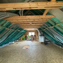 Poddasze w trakcie instalacji systemu wentylacji mechanicznej z rekuperacją, widoczne rury wentylacyjne, centrala rekuperacyjna, izolacja oraz drewniana konstrukcja dachu.