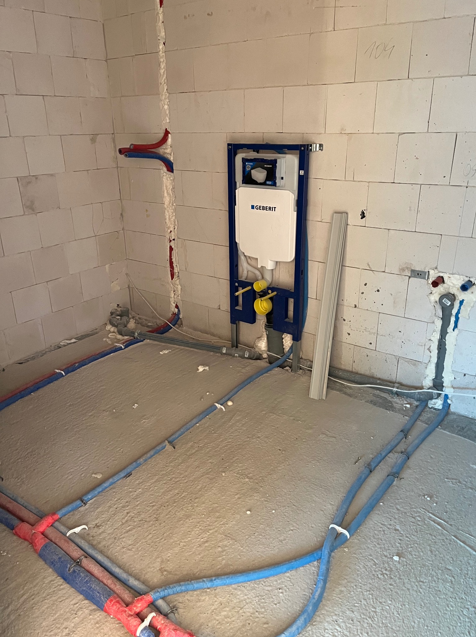 Wnętrze łazienki w trakcie remontu, widoczne rury instalacji wodnej i kanalizacyjnej w podłodze, stelaż podtynkowy Geberit zamontowany na ścianie z betonu komórkowego, podejścia wodne w ścianach...